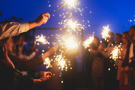 A crowd of young happy people with sparklers in their hands during birthday celebration