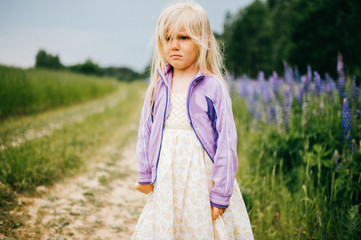 Fototapeta na wymiar Little cute child princess girl standing alone on road in wild terrain lost by parents. Tragic, sad, pathetic, expressive, offended emotions on face. Kid and baby teardrops. Lost and lonely blonde.