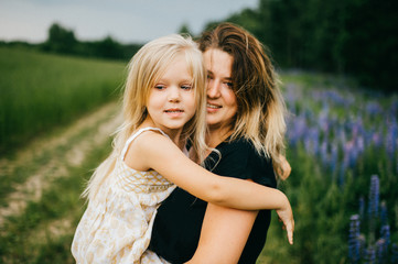 Fototapeta premium Young mother with long hair holding little daughter princess at hands. Playing with child. Pure, happy, kind, expressive emotional faces. Family at nature. Artistic kid. Laughing, smiling, embracing.
