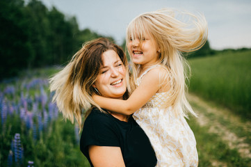 Fototapeta premium Young mother with long hair holding little daughter princess at hands. Playing with child. Pure, happy, kind, expressive emotional faces. Family at nature. Artistic kid. Laughing, smiling, embracing.