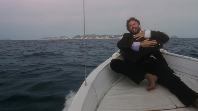 Happy man in suit hugging his briefcase sitting on the prow of a boat in the middle of the ocean