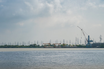 Fototapeta na wymiar Power plant crane situated near the river with cloudy sky background