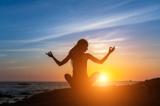 Yoga silhouette. Meditation woman on the ocean during amazing sunset.