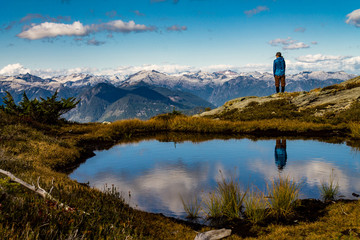 Girl looking at mountain in the alpine with her reflection in a small lake