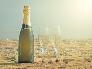 Two glasses and a bottle of champagne on a sandy beach on a hot summer day.