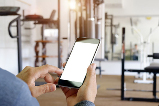 Man Hand Holding Smartphone Device At Gym Background.