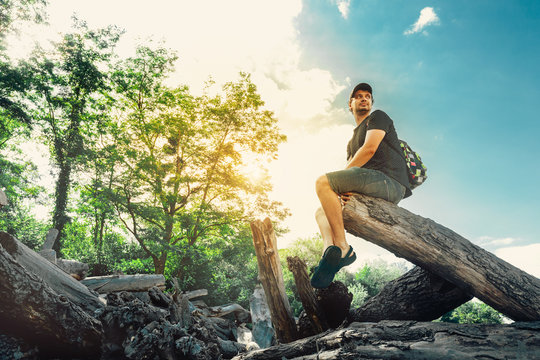 Young Hiker Man Resting On A Log In Summer Forest