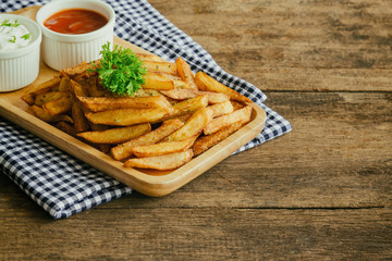 Homemade french fries serve with ketchup and sour cream or mayonnaise. Golden brown crispy french fries sprinkle with salt and oregano on wood plate for snack or appetizer. French fries on wood table.