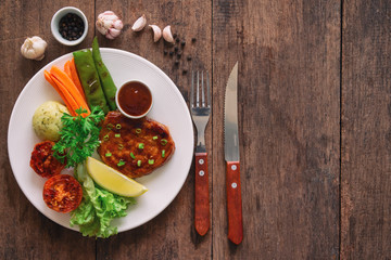 Barbecue pork steak on white plate served with barbecue sauce and vegetables. Pork steak for lunch or dinner on wood table. Moist and soft homemade pork barbecue served with mash potato and vegetable.