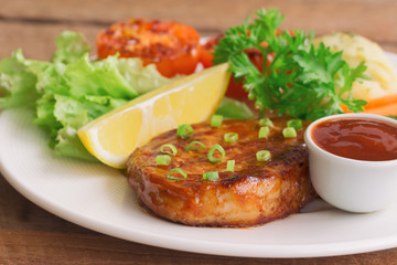 Barbecue pork steak on white plate served with barbecue sauce and vegetables. Pork steak for lunch or dinner on wood table. Moist and soft homemade pork barbecue served with mash potato and vegetable.