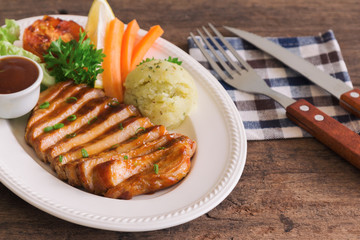Barbecue pork steak slices on white plate. Delicious pork steak for lunch or dinner on wood table. Moist and soft homemade pork barbecue served with mash potato barbecue sauce and vegetable.