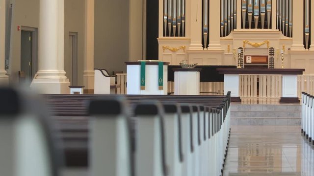 Panning shot of white church pews, with a pulpit, altar and pipe organ in background. Shot in 4K UHD.