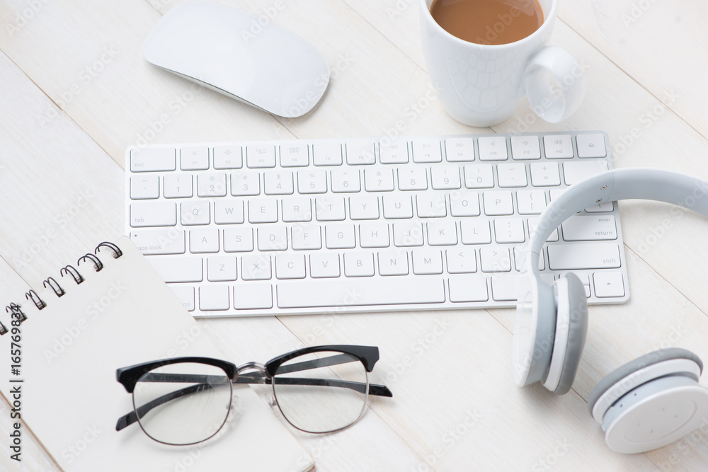 Poster notepad and computer on white table with headphone, eyeglasses, coffee cup. view from above