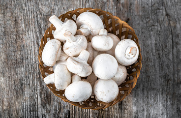 Fresh champignon mushrooms in a basket on wooden table, overhead