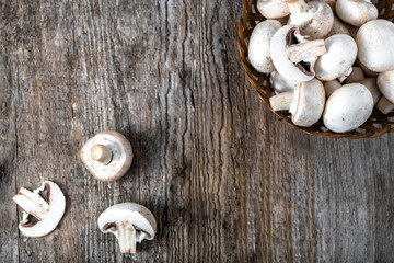 Fresh champignon mushrooms in a basket on wooden table, overhead