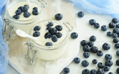 A tasty and healthy breakfast of fresh yogurt with blueberries in a small glass jar on a white wooden background.