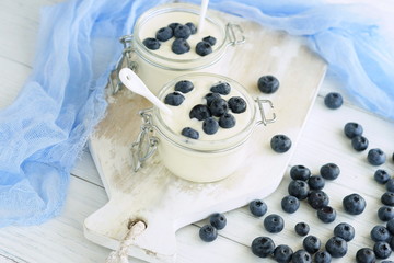 Obraz na płótnie Canvas A tasty and healthy breakfast of fresh yogurt with blueberries in a small glass jar on a white wooden background.