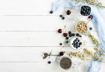 A tasty and healthy breakfast of fresh blueberries, granules, chia seeds, yogurt with blueberries in a glass jar on a white wooden background.Top view.Copy space