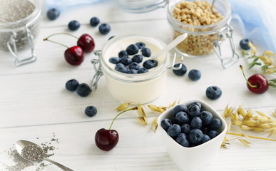 Naklejka na ściany i meble A tasty and healthy breakfast of fresh blueberries, granules, chia seeds, yogurt with blueberries in a glass jar on a white wooden background.