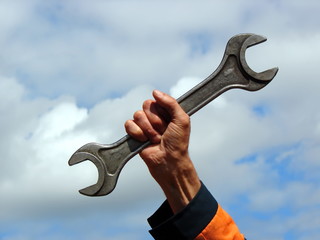 Hand with a large wrench on the sky background