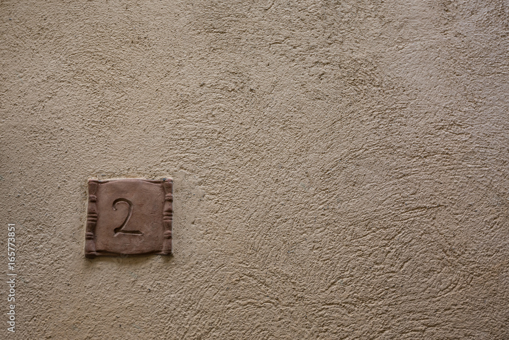 Wall mural road sign on a house reading the number two made out of brown ceramic.