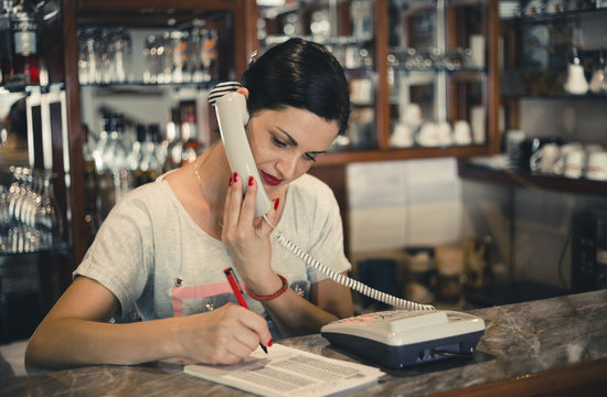 Young woman working at the pizzeria and writing order while talking on the phone