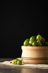 Juicy ripe berries of a gooseberry in a small wooden pot on black surface. Gooseberry harvest