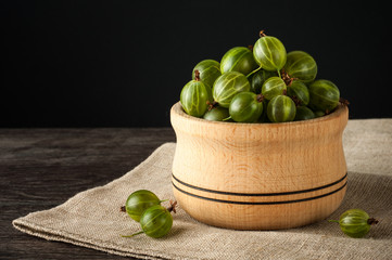 Juicy ripe berries of a gooseberry in a small wooden pot on black surface. Gooseberry harvest