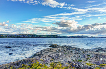 Landscape view of Saint Lawrence river from Ile D'Orleans, Quebec, Canada in summer with green plants, rocks and cityscape skyline of city and Levis town