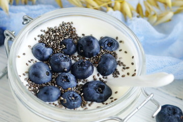 A tasty and healthy breakfast of fresh yogurt with blueberries and chia seeds in a small glass jar on a white wooden background.Close up