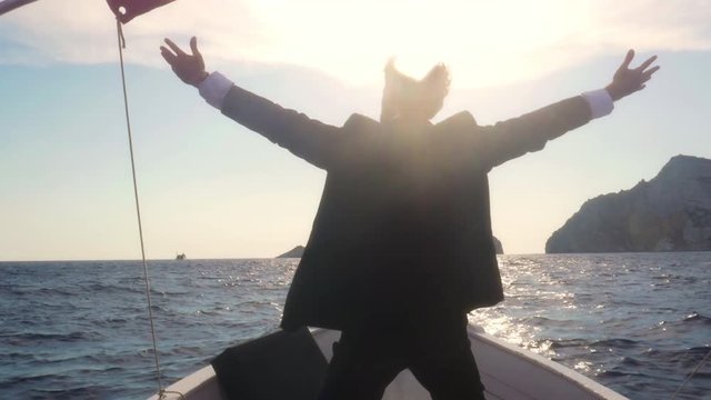 Happy man in suit with a briefcase exulting on the prow of a boat in the middle of the ocean