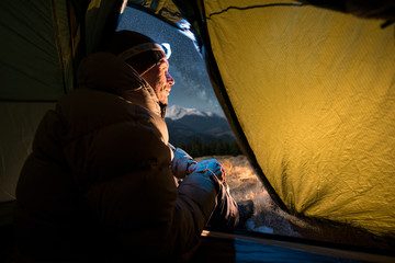 View from inside a tent on the male tourist have a rest in his camping at night. Man with a...