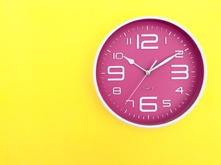 Closeup A pink wall clock set on yellow background. Top view with Copy space. Selective focus.