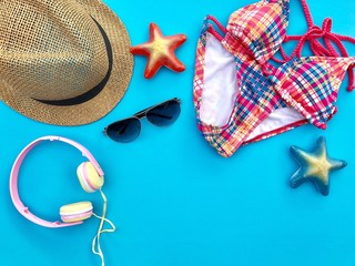 The concept of accessories for summer.CloseupA brown woven hat,sunglasses,pink headphone and colorful swimsuit with blue & orange starfish set on blue background.Copy space with Selective focus.