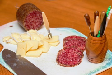 Homemade party preparation. Sliced salami and cheeses on white cutting board