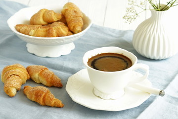 A white cup of coffee with milk and homemade sugar cookies bagels on blue linen tablecloth and white wooden table