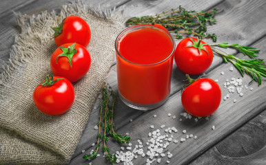 Freshly squeezed Tomato juice in glass. Ingredients for Tomato juice are crystalline salt, cherry tomatoes, rosemary greens and thyme on burlap. Rustic vintage gray wood background. 