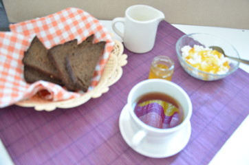 Breakfast on the table cup with tea milkwoman rye bread curds orange jam on a purple napkin