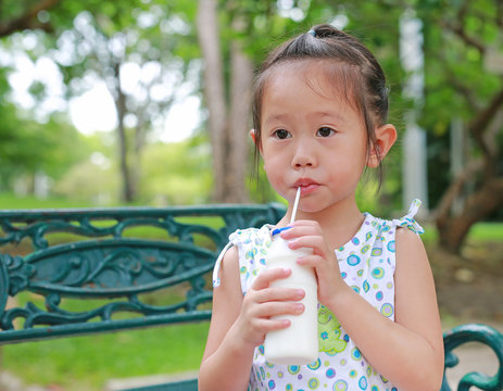 Little girl drinking milk with straw in the park.