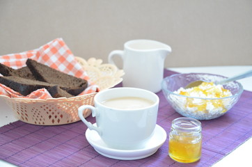Breakfast on the table cup with tea milkwoman rye bread curds orange jam on a purple napkin