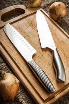 Two kitchen knives on an old wooden cutting board. European chef's knife and Japanese Santoku close-up