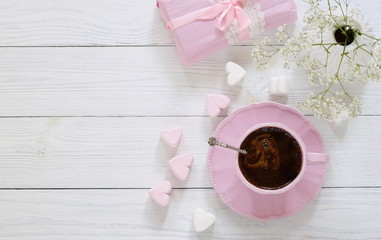 Fototapeta na wymiar Pink cup with coffee, marshmallows hearts and gift on a white wooden background.Top view. Copy space