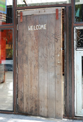 Welcome sign written by chalk on wood door background, open door.