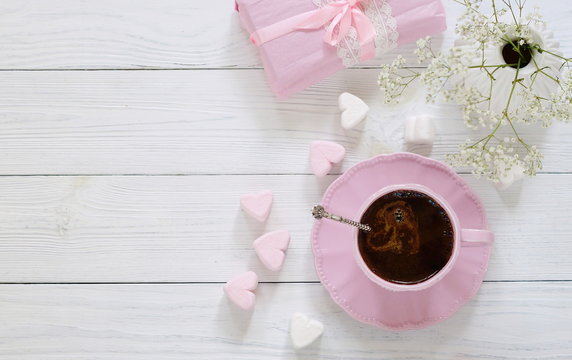 Pink cup with coffee, marshmallows hearts and gift on a white wooden background.Top view. Copy space
