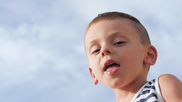 close up of little boy spitting with tongue out on sky background, slow motion