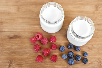 Yogurt in glass jar, raspberries and blueberries on a wooden background - from the top