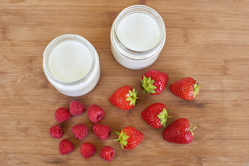Yogurt in glass jar, raspberries and strawberries on a wooden background - directly above