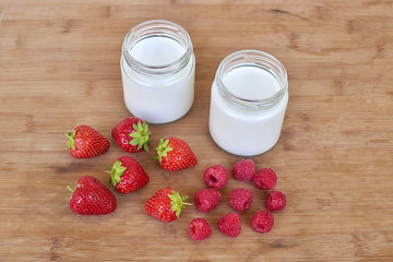 Yogurt in glass jar, raspberries and strawberries on a wooden background 