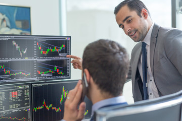 Businessmen trading stocks online. Stock brokers looking at graphs, indexes and numbers on multiple...