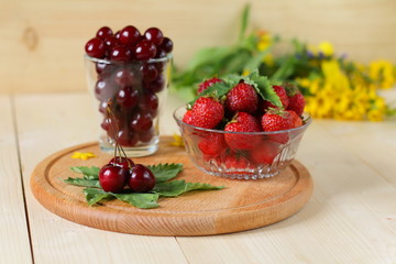 Fresh cherries and strawberries are on a wooden background.